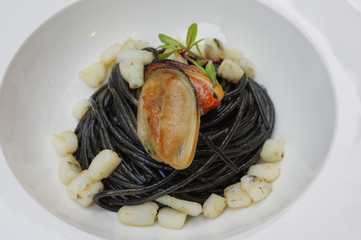 Squid ink black pasta with mussel meat in white bowl plate at Italian cuisine restaurant