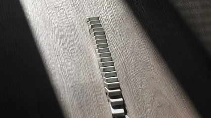 A men pushes a Domino and starts a chain reaction on the floor in a patch of sunlight. Sun ray. Close-up. Slow motion. Dominoes. Chain reaction. The Domino Principle. Board game. Falling dominoes.