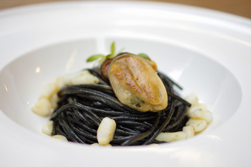 Black squid ink pasta with mussel meat in white bowl plate in Italian cuisine restaurant