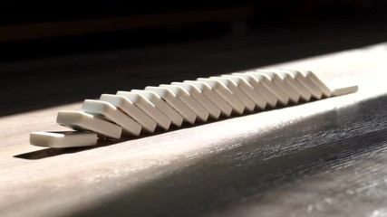 A men pushes a Domino and starts a chain reaction on the floor in a patch of sunlight. Sun ray. Close-up. Slow motion. Dominoes. Chain reaction. The Domino Principle. Board game. Falling dominoes.