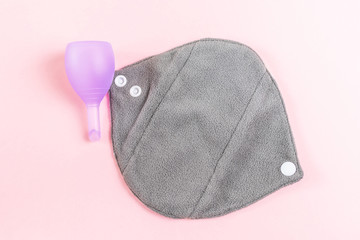Reusable eco-friendly female pad made of natural fabric with fleece for every day and a menstrual cup. Pink background, place for text, minimalism, top view, flat lay. Zero waste concept