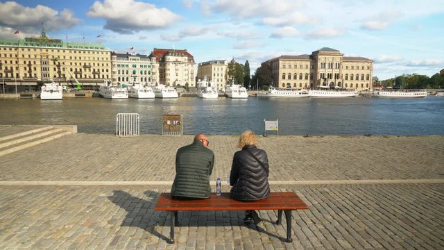 Tourists on bench in Stockholm with a view of beautiful cityscape looking at map.