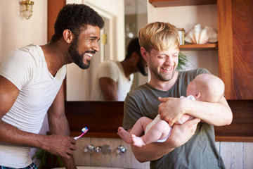 Loving Male Same Sex Couple Cuddling Baby Daughter In Bathroom At Home Together