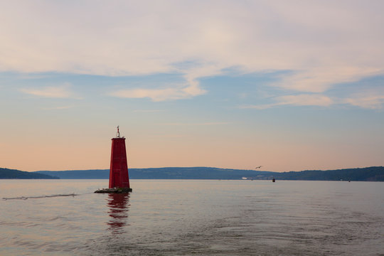 A large red buoy marks the entrance of Cayuga Inlet off Cayuga Lake, in Ithaca, New York State in the Finger Lakes Region during a calm sunset.  - Powered by Adobe
