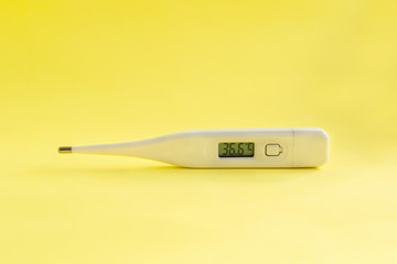 Digital medical thermometer with temperature of 36.6 on light yellow background.