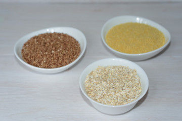 three cereals-buckwheat, oatmeal and millet. in white plates on a wooden background. healthy diet. full diet food