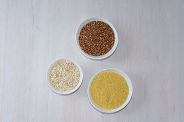 three cereals-buckwheat, oatmeal and millet. in white plates on a wooden background. healthy diet. full diet food