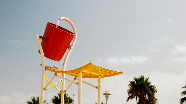 Water poured from huge bucket over people at water park, slow motion