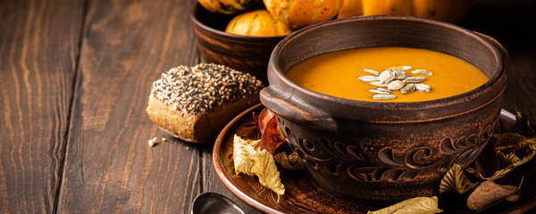 Vegetarian autumn roasted pumpkin and carrot cream soup with seeds in old brown bowl. Healthy food concept with copy space, banner