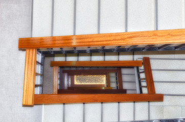 Stairwell. Indoor view. Handrail of wood. Stairs covered of gray carpet. White stones, at the background, illuminated with soft warm light.