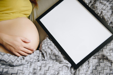 Pregnant girl blonde in a yellow T-shirt at home. Waiting for a miracle. Pregnancy. Love and hope. Light room. Lies in bed in the bedroom. Frame for text. Gray bedding.
