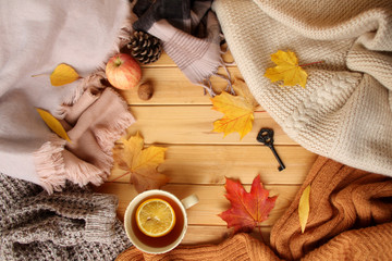 cup of hot fragrant tea with lemon, autumn leaves, apple, cozy scarves and knitted sweaters, key, flat, concept of hugg, winter or autumn mood