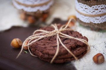 Hazelnuts in the peel and oatmeal cookies on brown table.  Oatmeal cookies  with crack pattern and nuts on  table in rustic style. Baking is folded in a row on each other and tied with natural braid. 