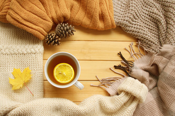 cup of hot fragrant tea with lemon, autumn leaves, apple, cozy scarves and knitted sweaters, flat, concept hugge, winter or autumn mood