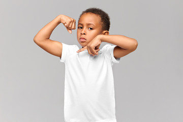 Horizontal shot of confident serious Afro American boy of school age posing isolated at gray studio...