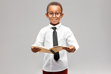Studio image of funny smart akward African schoolboy in formal clothes and eyeglasses eager to...