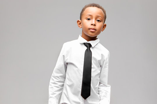 Isolated image of handsome confident African American schooler in clean ironed white shirt and elegant black tie posing against gray studio wall background with copy space for your advertising content