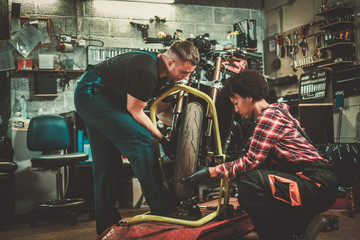 Fototapeta na wymiar Mechanic and his helper repairing a motorcycle in a workshop