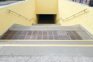 Empty yellow underground pedestrian crossing. Tunnel and daylight at the end. Steps to the top at...