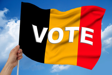 hand holds against the background of the sky with clouds the colored flag of Belgium on the texture of the fabric, silk with waves, close-up, with the word vote