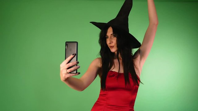 Young beautiful woman in red dress and witch hat makes selfie. Halloween.4k
