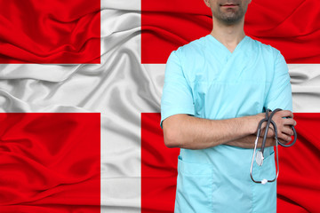 male doctor in uniform professional clothes with a stethoscope stands against the background of the national flag, the concept of the country's health and medical insurance, close-up, copy space