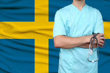 male doctor in uniform professional clothes with a stethoscope stands against the background of the national flag, the concept of the country's health and medical insurance, close-up, copy space
