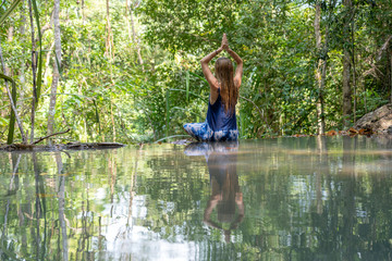 Beautiful woman practicing yoga near turquoise water of cascade waterfall at deep tropical rain forest, island Koh Phangan, Thailand