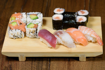 mix of sushi, sushi roll and nigiri with salmon, tuna, sea bass, shrimp, avocado served on a wooden plate