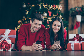 Close up photo of two romantic people use cell phone lying on floor with git boxes enjoy christmas...