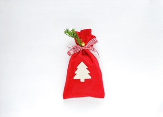 Red Christmas gift bag, decorated with white Christmas tree, ribbon, green branch and jingle bell on white background.