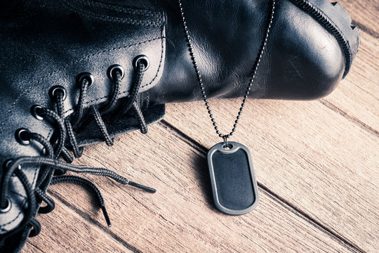 Black rubber edge military dog tag with some part of black genuine leather combat boots on the old wooden floor