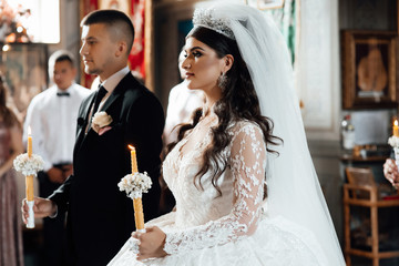 Couple in church. Bride and groom hold shiny candles during the ceremony in church. Hands of...