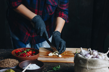 Woman hands in black gloves chopping garlic