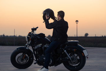 Fototapeta na wymiar Biker man with his custom motorcycle putting on a helmet at sunset