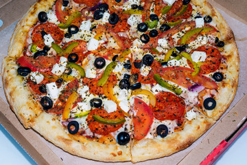 Fragrant delicious Greek pizza in a cardboard box on a light background. The view from the top. Order for a group of friends.