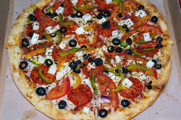 Fragrant delicious Greek pizza in a cardboard box on a light background. The view from the top. Order for a group of friends.