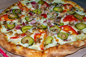 Fragrant tasty pizza with pickled cucumber in a cardboard box on a light background. Top view. Order for a group of friends.