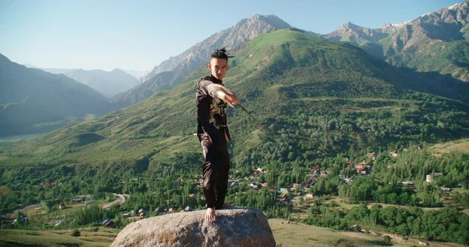 Young man practicing kung fu with sword. Tai Chi at the top of the mountain. Sword of the Shaolin monk. 4K Slow motion.