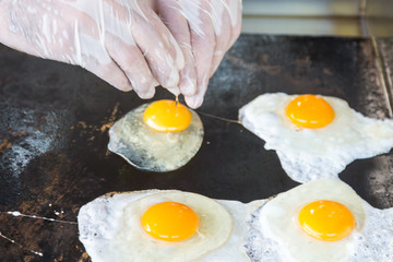 A man in white gloves fries eggs. The cook breaks egg and pours it into the pan