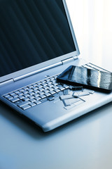 A silver laptop with a broken keyboard and a tablet with a cracked display. A close-up picture of part of broken laptop and cracked screen on a tablet.
