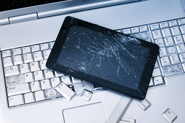 A silver laptop with a broken keyboard, tablet with a cracked display and black phone. A close-up...