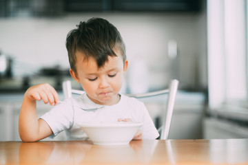 Naklejka premium A little boy in the kitchen eating oatmeal from a white plate