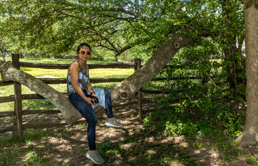 Woman sitting on branch of tree in front of pasture