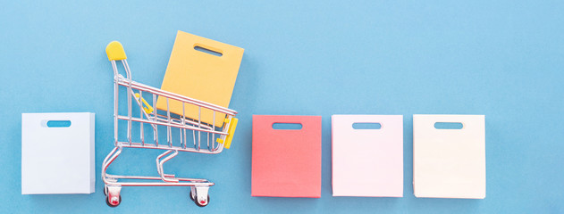 Abstract design element, concept of annual sale, shopping season - mini yellow cart with paper bag isolated on pastel blue background, top view, flat lay. © RomixImage