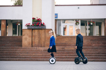 Two young schoolchildren  riding on gyroscooters.  Kids go to school for gyroscooters. Blonde kids....