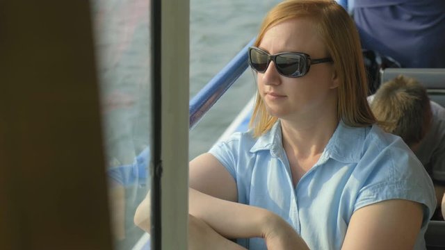woman in sunglasses on a boat sits. She is happy admiring the beautiful scenery