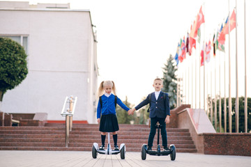 Two young schoolchildren  riding on gyroscooters.  Kids go to school for gyroscooters. Blonde kids....