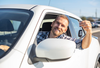 A man in a white car shows a key. Buying or renting a car - concept.