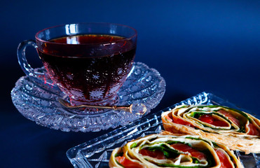 Cup of tea and snack of salmon and greens on dark background.